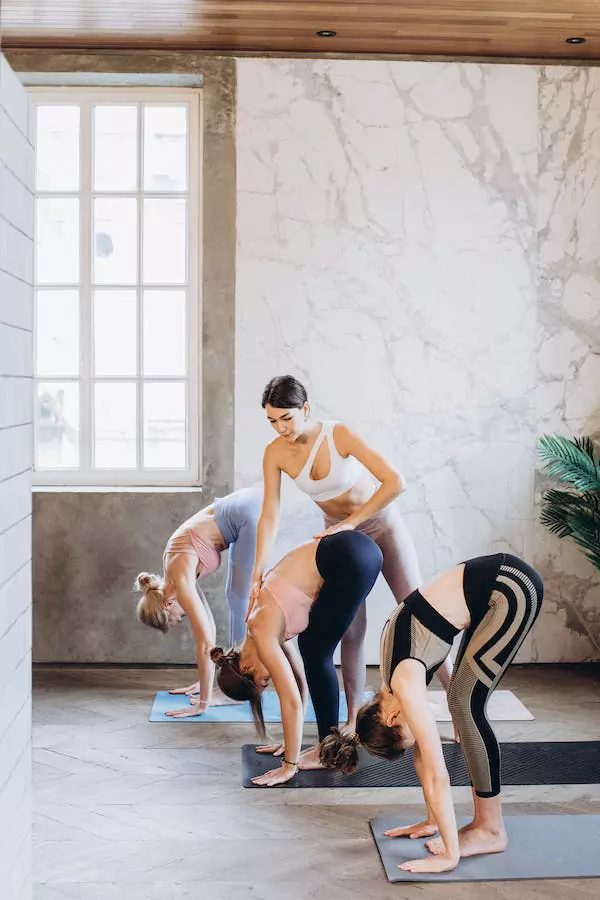  A lady yoga instructor helping students with their yoga poses.